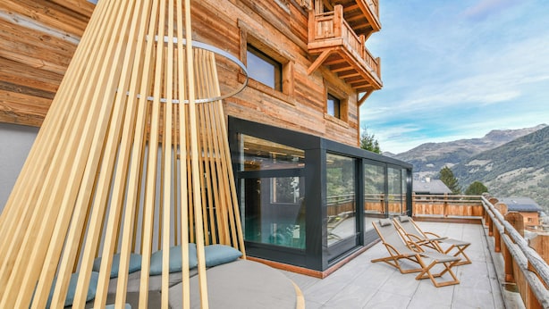 Eine Holzhütte mit Balkon, einer modernen Glasdoor und Blick auf die Berge.