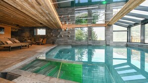 Ein moderner, überdachter Innenpool mit Glasdach, Holzboden und Blick ins Freie.