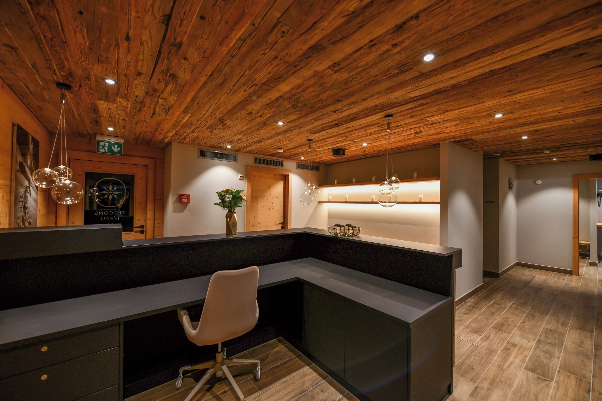 A reception area with a wooden ceiling, a reception desk, a white office chair, and a plant.