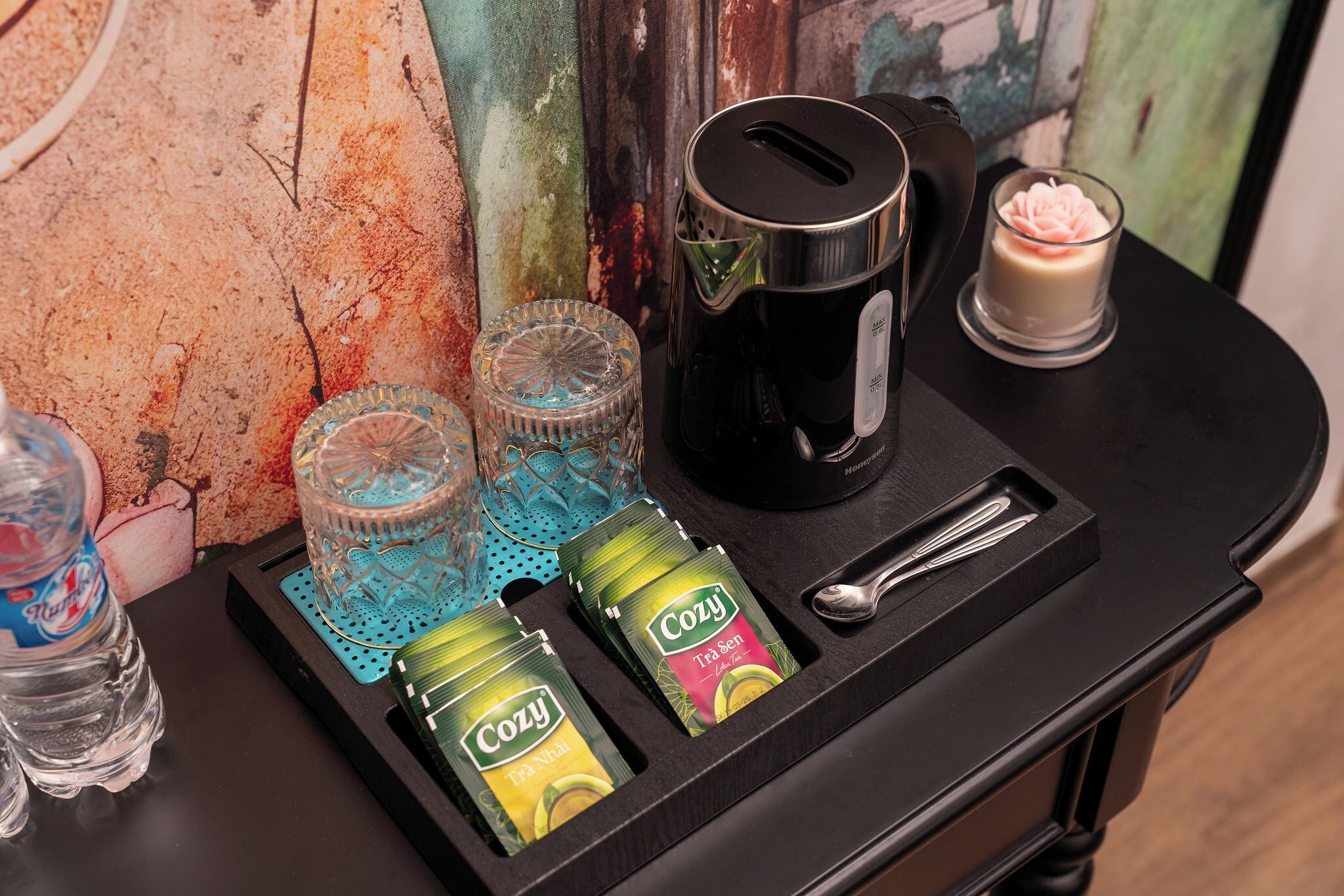 A tray with a water bottle, two glass tumblers, a coffee maker, a spoon, and two packets of tea.