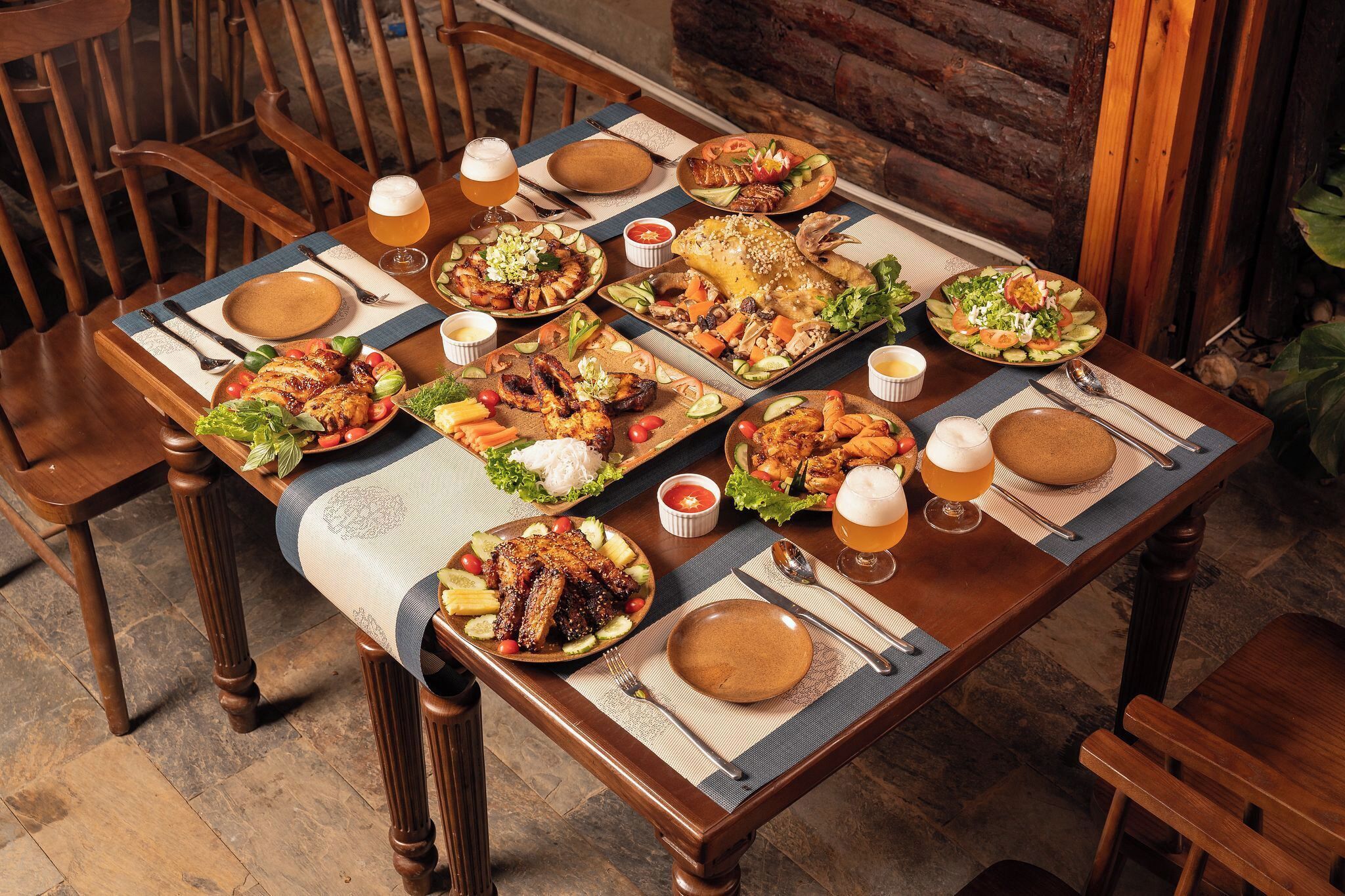 Een houten eettafel gedekt met verschillende gerechten, drankjes en bestek.