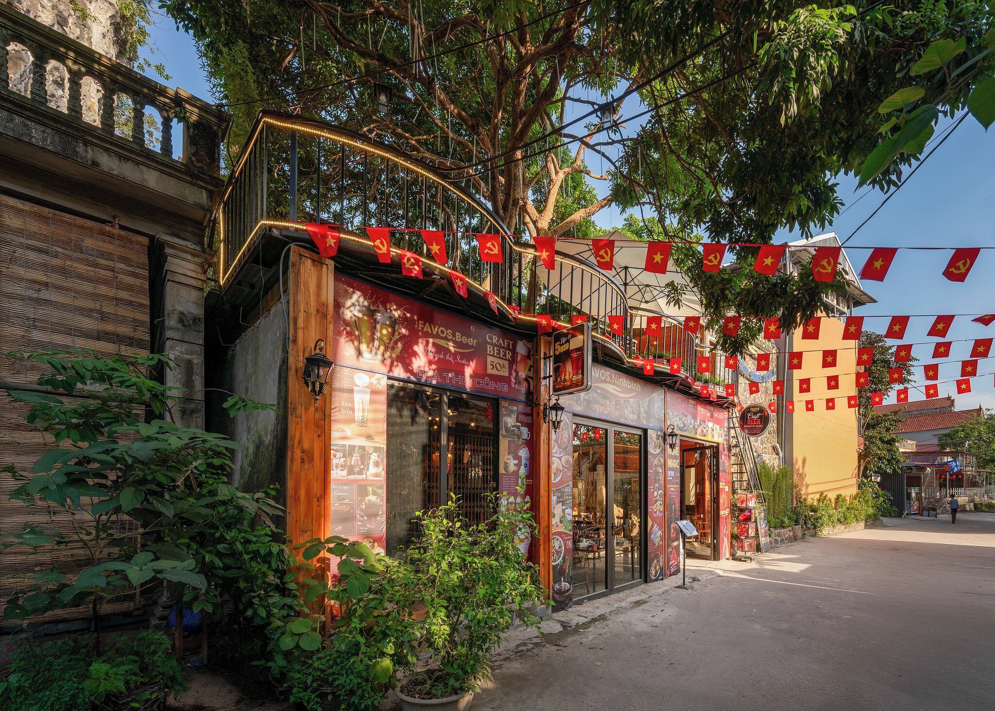 A restaurant with outdoor seating, red banners, and a traditional architectural style.