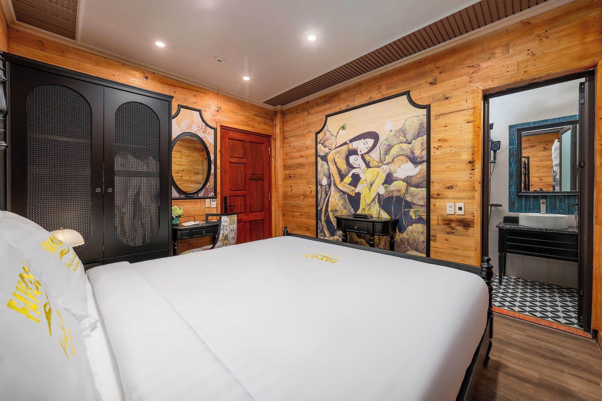 A hotel room with a large bed, wooden walls, a wooden door, a mirror, a sink, and a small table.