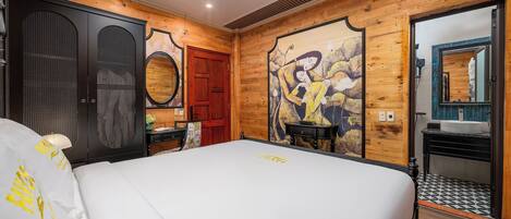 A hotel room with a large bed, wooden walls, a wooden door, a mirror, a sink, and a small table.