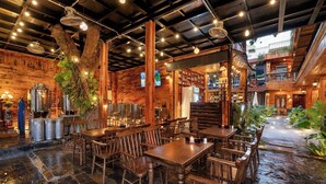 A rustic interior with wooden tables and chairs, a stone floor, and a central staircase leading to an upper level. - Favos Ninh Binh Hotel & Villas (Nam Hoa Lu)