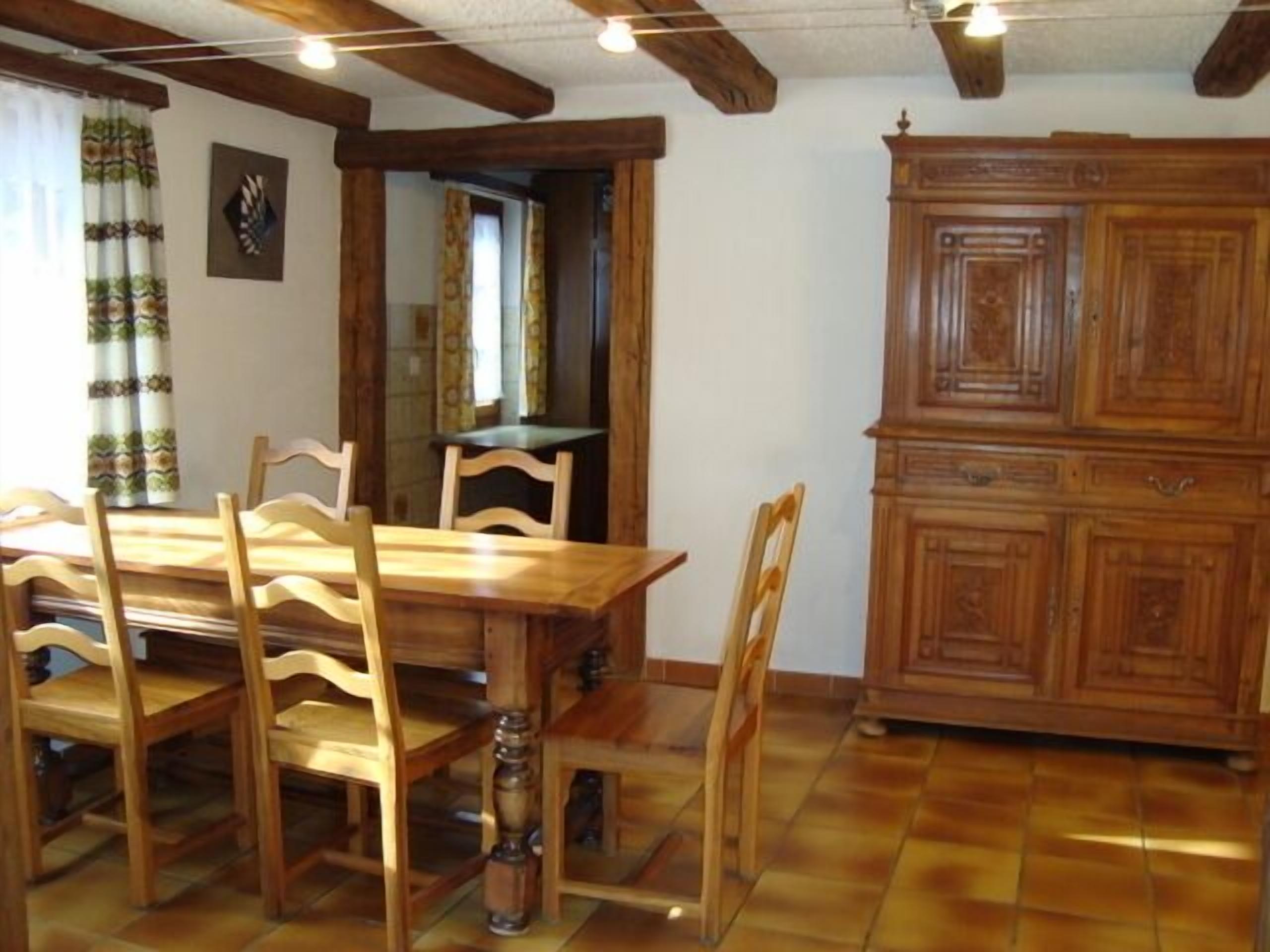 A dining area with a wooden table and chairs, a cabinet, and a tiled floor.