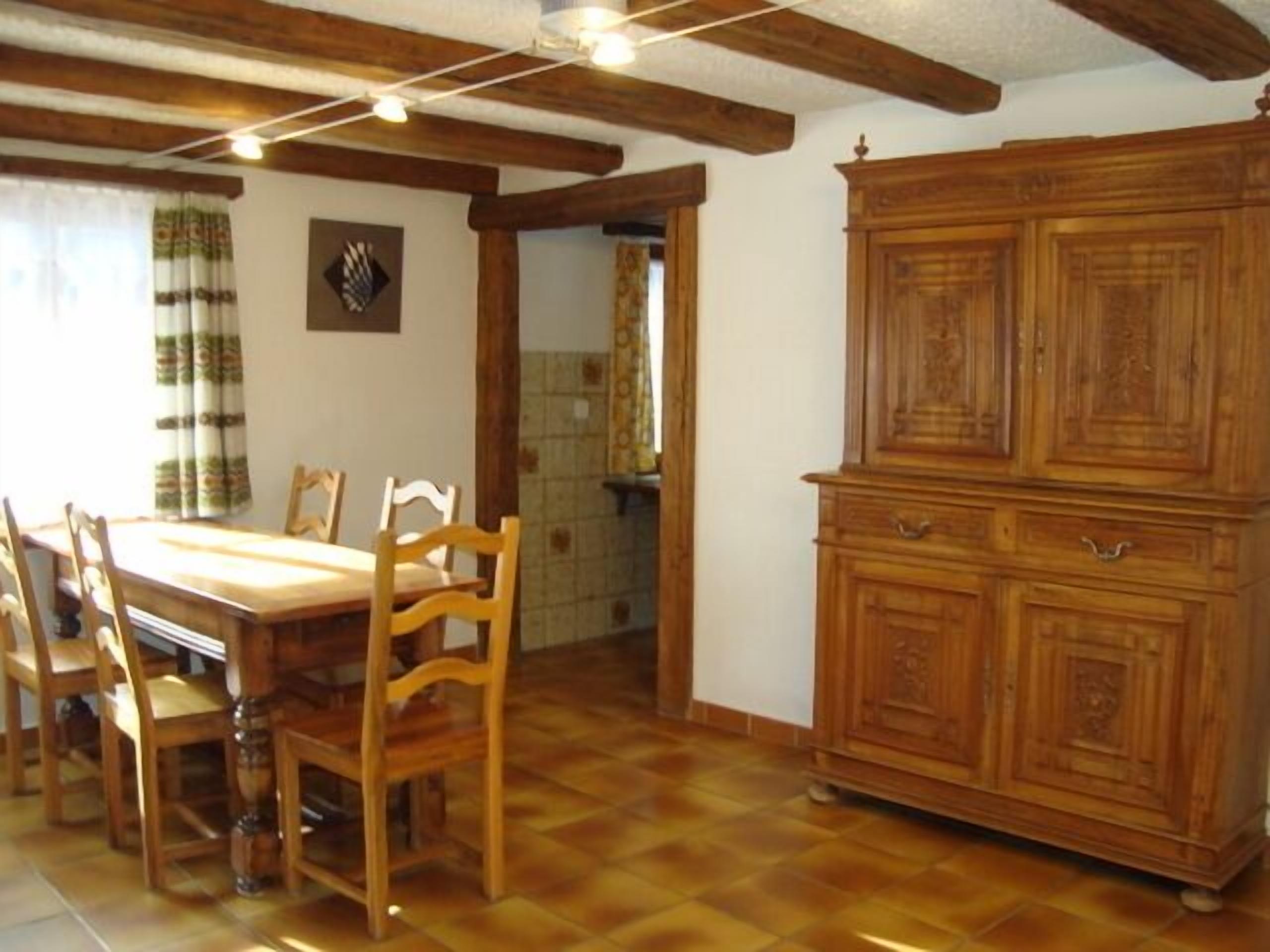 Zona pranzo con tavolo e sedie in legno, un armadietto in legno e pavimento piastrellato.