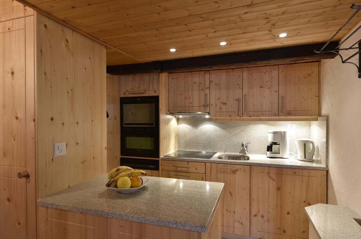 Une cuisine avec des meubles en bois, des plans de travail en granit, une cuisinière et une machine à café.