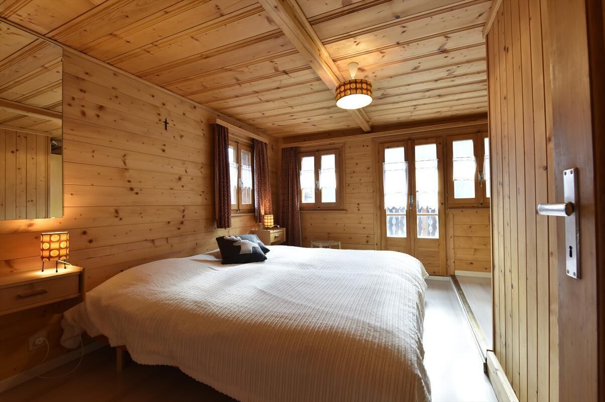 Une chambre à coucher dans une cabane en bois, avec un grand lit, une table de chevet avec une lampe et une fenêtre avec des rideaux.