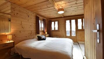 Une chambre à coucher dans une cabane en bois, avec un grand lit, une table de chevet avec une lampe et une fenêtre avec des rideaux.