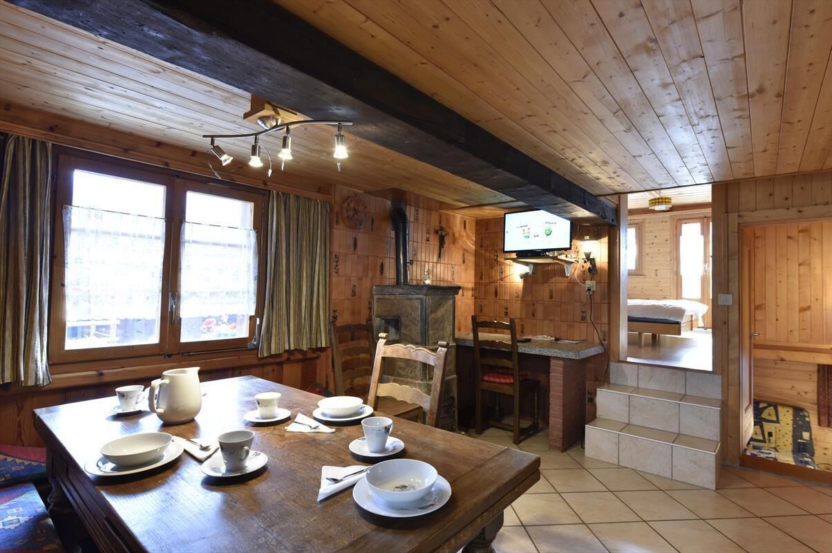 Interior de una cabaña de madera con una mesa de comedor preparada para cuatro personas, una chimenea y un televisor.
