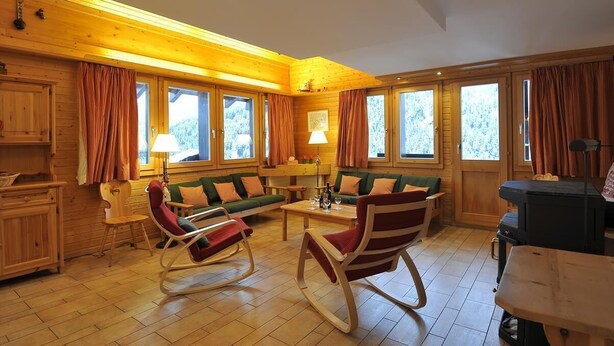 Ein gemütliches Blockhaus-Interieur mit Holzwänden, einem grünen Sofa, Schaukelstühlen und einem Esstisch.
