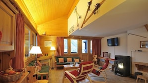 Ein gemütliches Blockhaus-Interieur mit Holzwänden, einer Couch, Schaukelstühlen, einem Kamin und einem Fernseher.