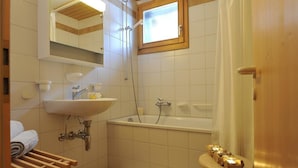 Ein Badezimmer mit Waschbecken, Spiegel, Dusche und einem kleinen Hocker mit Kerzen.