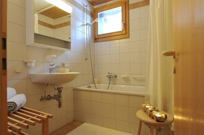 Ein Badezimmer mit Waschbecken, Spiegel, Dusche und einem kleinen Hocker mit Kerzen.