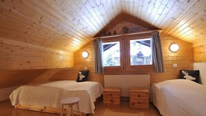 Ein gemütliches Cabin-Zimmer mit zwei Betten, einem kleinen Hocker und einem Fenster mit Vorhängen.
