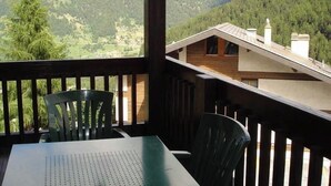 Ein Balkon mit Tisch und Stühlen, der auf eine gebirgige Landschaft mit einer Holzhütte im Hintergrund blickt.
