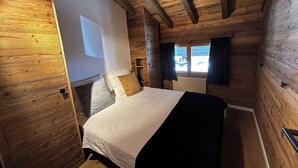 Ein Schlafzimmer einer Holzhütte mit Bett, Kissen und einem Fenster mit Vorhängen.
