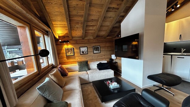 Ein modernes Wohnzimmer mit einer Couch, schwarzen Sesseln, einem Couchtisch und einem Fernseher.