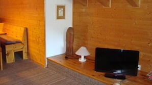Ett rum med träpanel, en säng, ett skrivbord med en lampa och en tv.