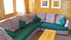 Ett mysigt rum med en grön, modulbaserad soffa, ett soffbord i trä och två inramade konstverk på den träpanelbeklädda väggen.
