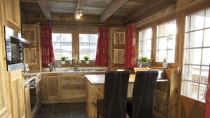 A rustic kitchen with wooden cabinets, a central island, and a dining area with chairs. - Chalet Jean - Grimentz - Beautiful traditional Swiss chalet for 2 to 12 people<br>Luxury 3-storey chal (Grimentz)