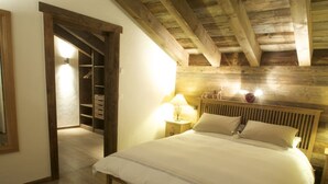 A bedroom with a wooden ceiling, a large bed with white bedding, a nightstand with a lamp, and a wooden wardrobe. - Chalet Jean - Grimentz - Beautiful traditional Swiss chalet for 2 to 12 people<br>Luxury 3-storey chal (Grimentz)