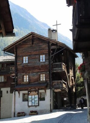 Ein rustikales Holzhaus mit Balkon, Kruzifix und Bergblick.