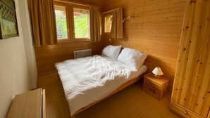 Une chambre dans une cabane en bois, avec un lit, une table de chevet, une fenêtre et un radiateur.