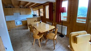 Un intérieur en bois comprenant une table et des chaises, un coin cuisine et une vue dégagée grâce à de grandes fenêtres.