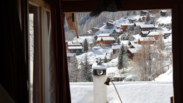 Un village de montagne enneigé, avec des maisons en bois et une église recouverte de neige.
