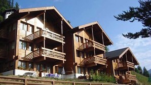 Un chalet en bois doté de plusieurs balcons et d’un toit en pente, situé sur une colline.