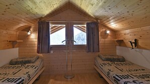 Una cabaña acogedora con dos camas, paredes de madera, techo inclinado y una ventana con cortinas.
