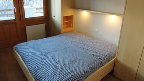 Ein Einzelbett mit karierter Bettdecke in einem Zimmer mit Holzwänden und -schränken.