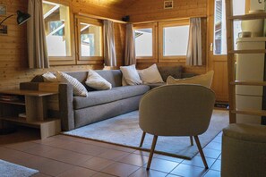 Ein gemütliches Blockhausszimmer mit einer Couch, einem Sessel und einem Holzregal.
