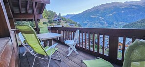 Um deck de madeira com mesa e cadeiras, com vista para uma paisagem montanhosa.