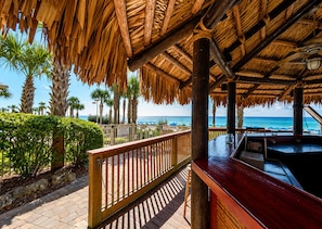 Eine Holzterrasse mit einem Reetdach mit Blick auf einen Strand.