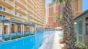 Een zwembadgedeelte van een hotel, met een helderblauw zwembad, een pergola en een palmboom.