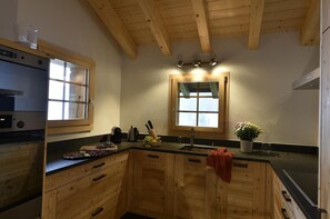 Eine Küche mit Holzausstattung, einem Einbauofen, einem Spülbecken und einem Fenster mit Spiegel darüber.