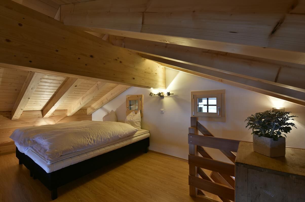 Um pequeno quarto no sótão, com uma cama, escada de madeira e um vaso de planta.