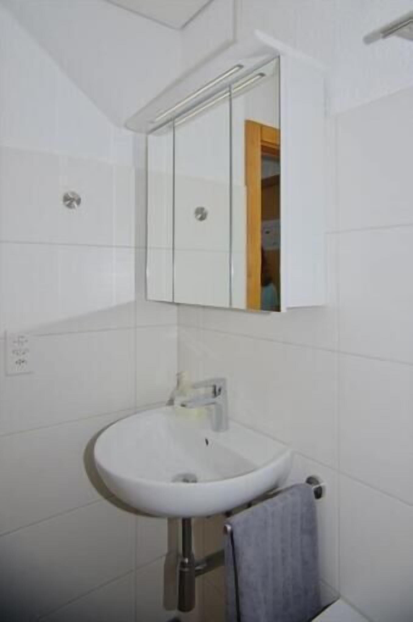 Un baño con un lavamanos blanco, un espejo y un perchero para toallas.