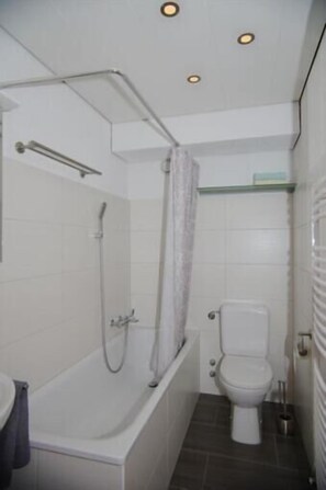 Ein kleines, modernes Badezimmer mit einer weißen Badewanne, einer Dusche und einem WC.