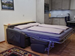 Ein kleines Zimmer mit Bett, Küchenzeile und Teppich.