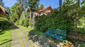 Un sentiero conduce a una casa con una panchina di legno, immersa nel verde e alberi.