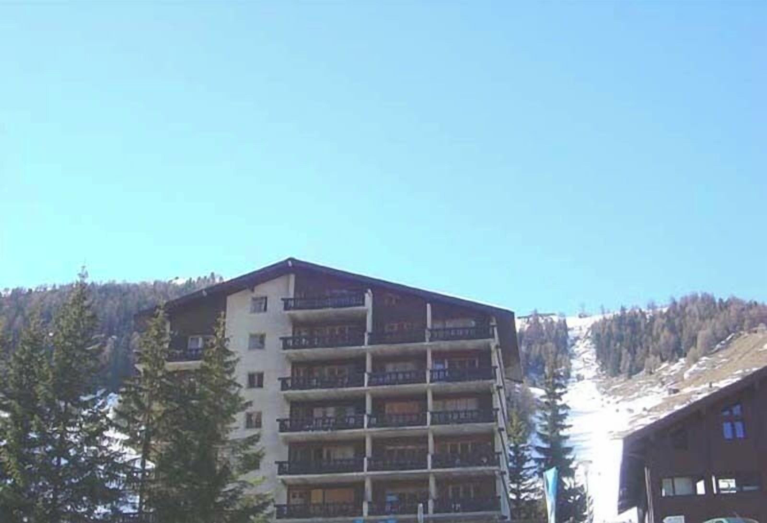 Un hôtel à plusieurs étages doté de balcons, entouré d’arbres et avec une chaîne de montagnes en toile de fond.