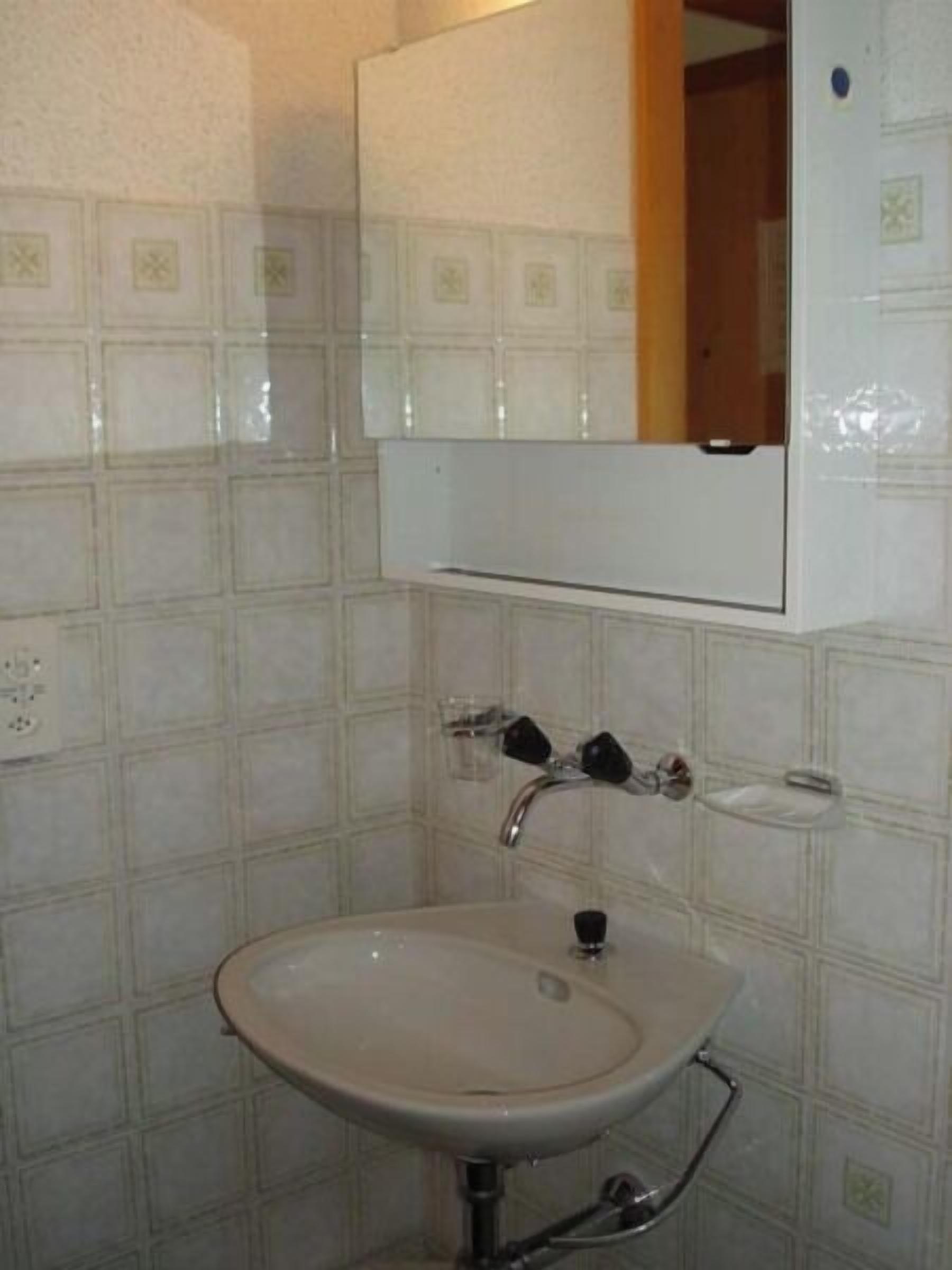 Un bagno con un lavandino bianco, uno specchio sopra e pareti piastrellate.