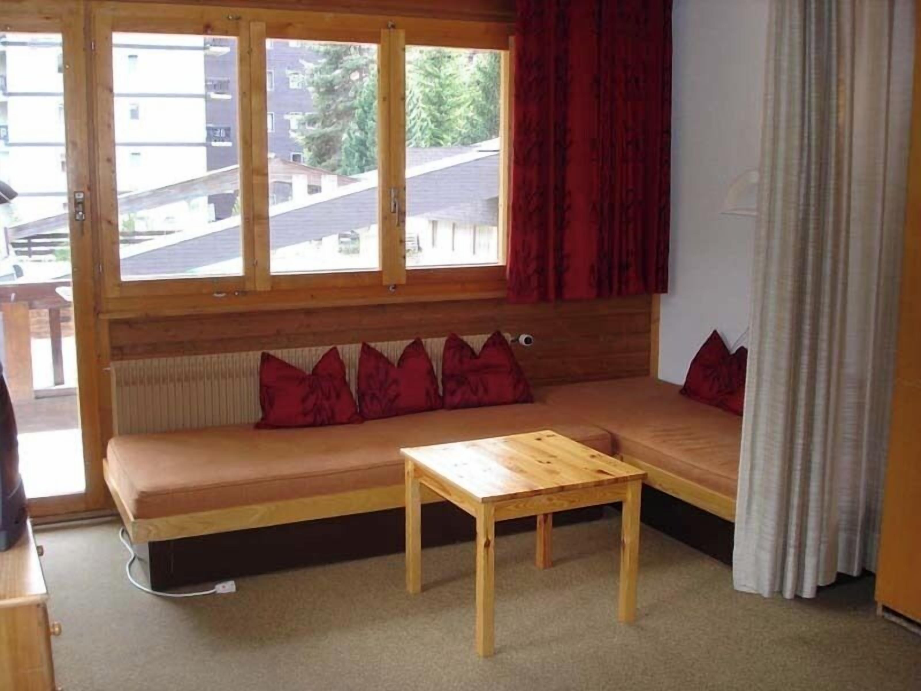 A cozy room with a wooden bench, a small table, and a window with red curtains.