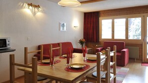 A dining area with a wooden table set for four, red upholstered chairs, a wooden ceiling, and a window with curtains. - Comfortable 3-room apartment for 4-6 persons : Living room with double sofa-bed - 1 room with 2 beds (Grimentz)