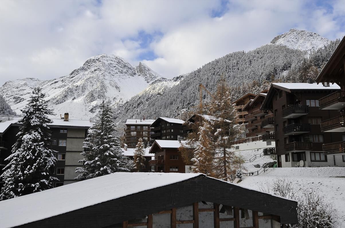 A snow-covered mountain resort with multiple chalet-style buildings, wooden balconies, and a ski lift visible in the background.