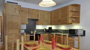 A modern kitchen with wooden cabinets, a dining table set for four, and a microwave on the countertop. - Comfortable 3-room apartment for 4-6 persons : Living room with double sofa-bed - 1 room with 2 beds (Grimentz)